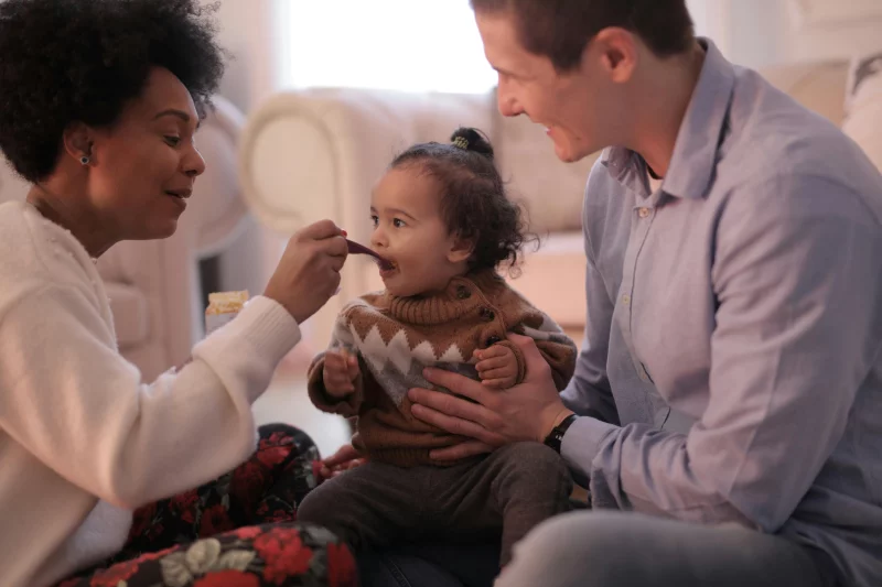 A heartfelt moment of a family feeding their cheerful toddler in a cozy living room setting.