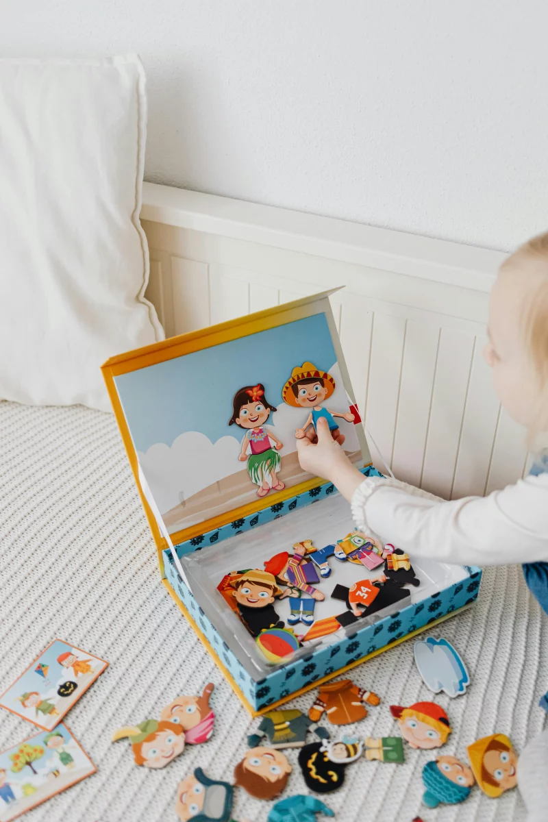 A young girl playing with a vibrant dress-up puzzle set on a bed, featuring cartoon characters.