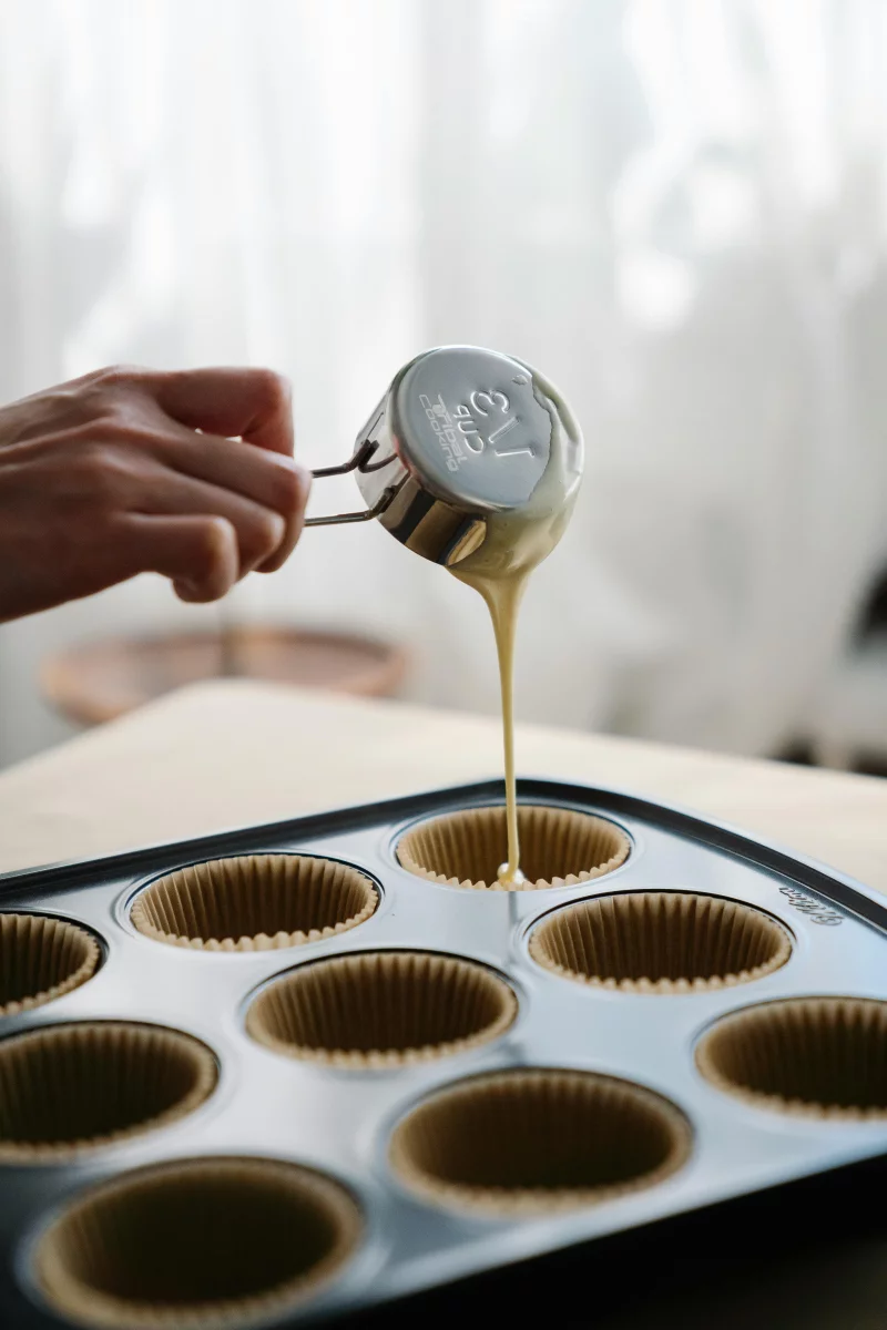 Close-up of pouring batter into muffin liners on a baking tray, indicating homemade baking.