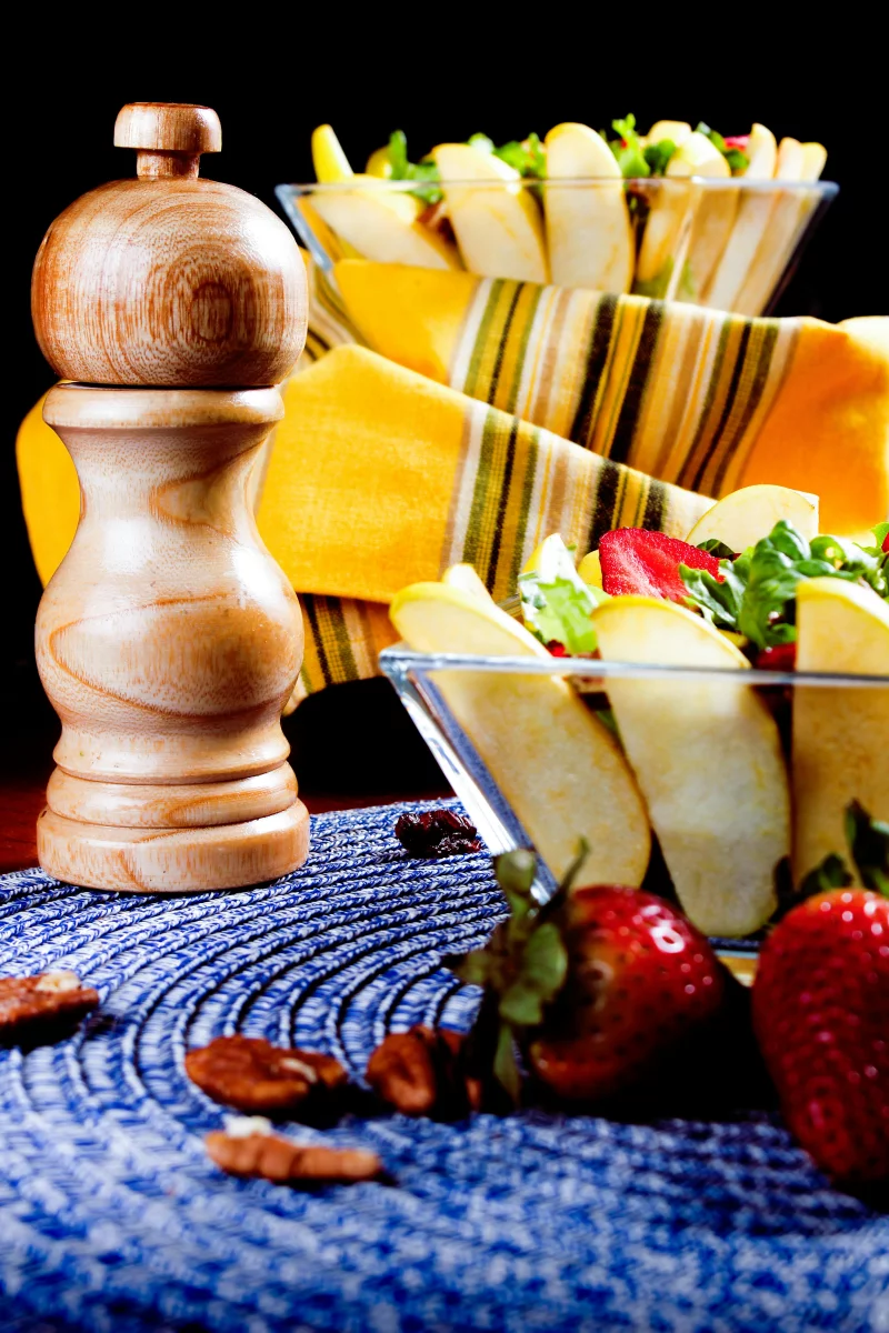 Healthy salad with apples, strawberries, and pepper mill on stylish table setting.