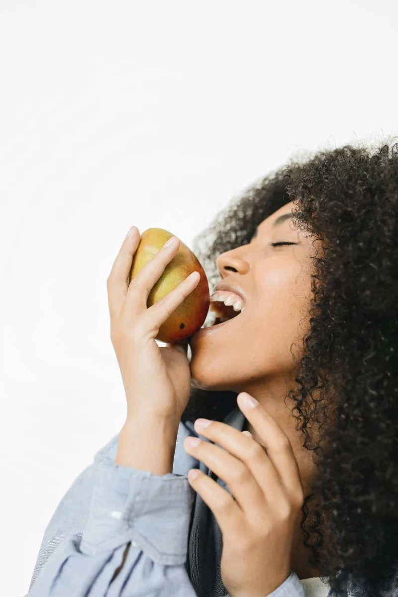 A woman enjoys a fresh mango, embodying healthy eating and happiness.