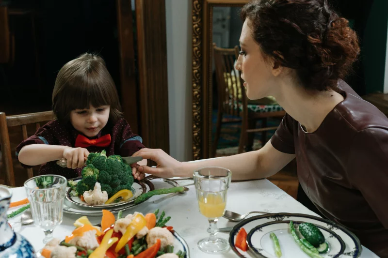 A young boy and a woman sharing a meal with vegetables, promoting healthy eating habits.