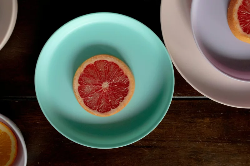 Top view of wooden table with ceramic plates with sliced ripe red grapefruits in light place