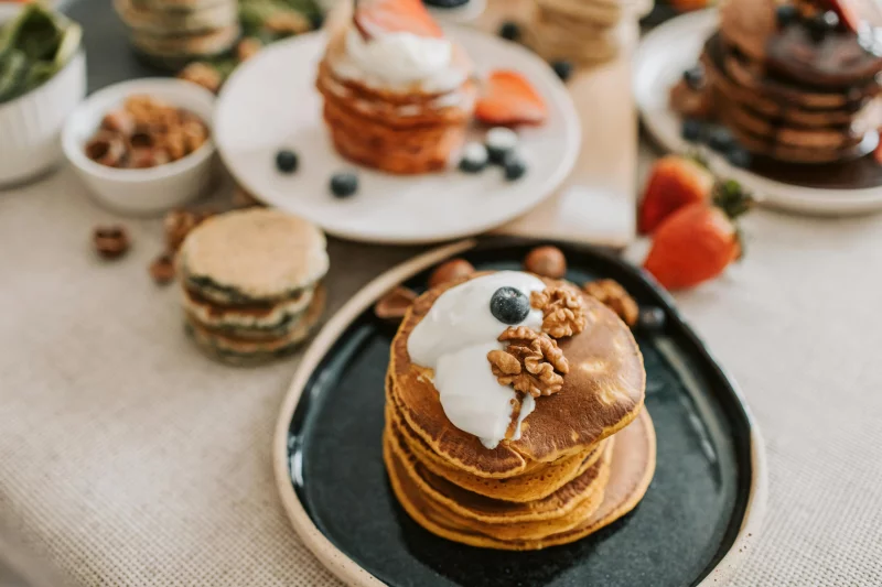 A stack of pancakes topped with yogurt, walnuts, and blueberries, perfect for a mouthwatering breakfast.