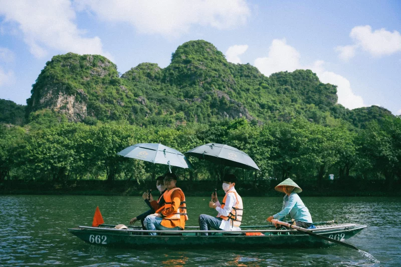 People enjoying a scenic boat ride in Ninh Bình, Vietnam, surrounded by lush mountains.