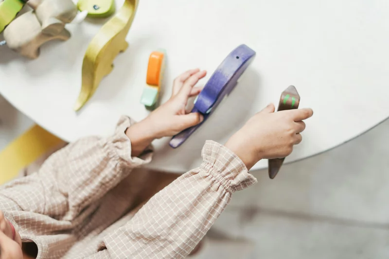Top view of a child playing with colorful wooden toys, focusing on hands and table.