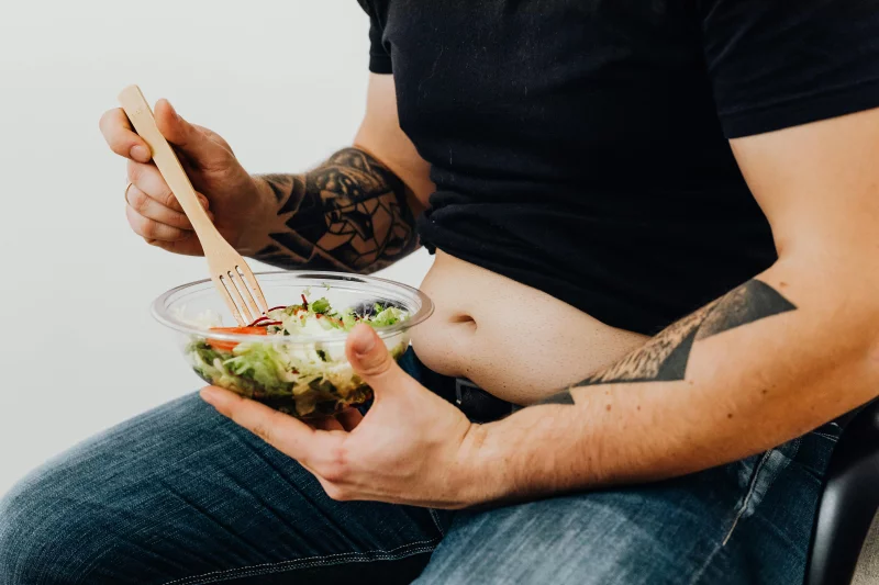 A tattooed individual holding a fresh salad, symbolizing healthy lifestyle and fitness motivation.