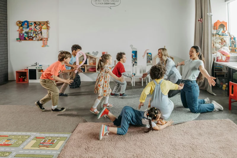 Joyful children and teachers playing together in a colorful classroom setting.