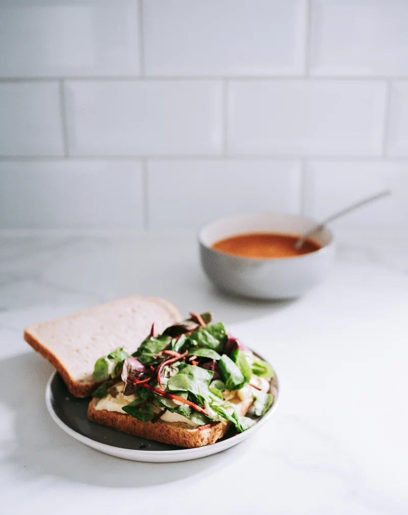 A delicious and nutritious open-faced sandwich with greens, served with soup in a modern setting.