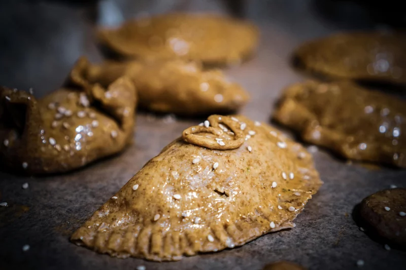Close-up of rustic homemade pastries with sesame seeds, showcasing golden brown dough and a delicious finish.