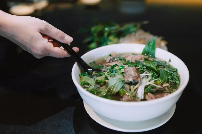 Close-up of a hand holding chopsticks over a bowl of flavorful Vietnamese pho.
