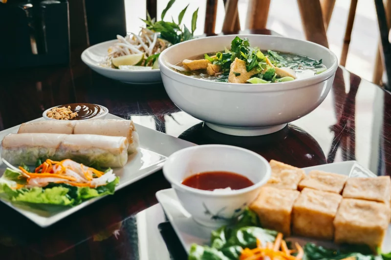 A delicious spread of Vietnamese dishes including pho, spring rolls, and tofu displayed on a wooden table.