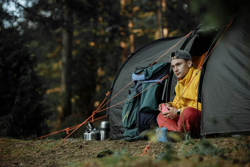A young man enjoys the outdoors at a campsite, surrounded by camping gear and nature.