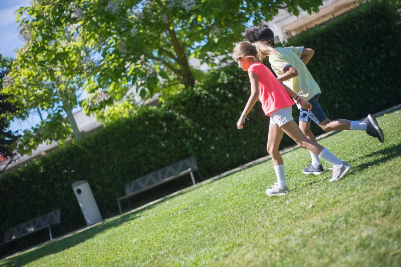 Two kids enjoying outdoor play in a sunny park with greenery.