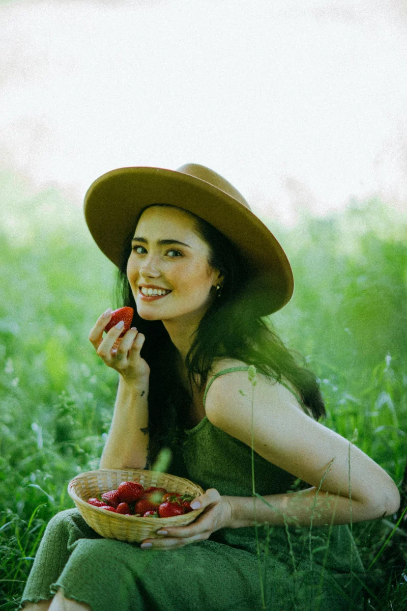 A joyful moment with a woman holding strawberries in a sunny green field.