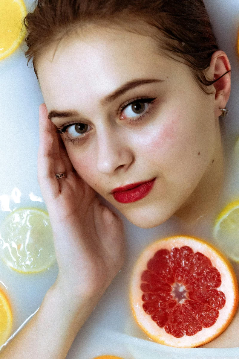 Elegant photo of a woman in a milk bath surrounded by citrus slices, highlighting beauty and freshness.
