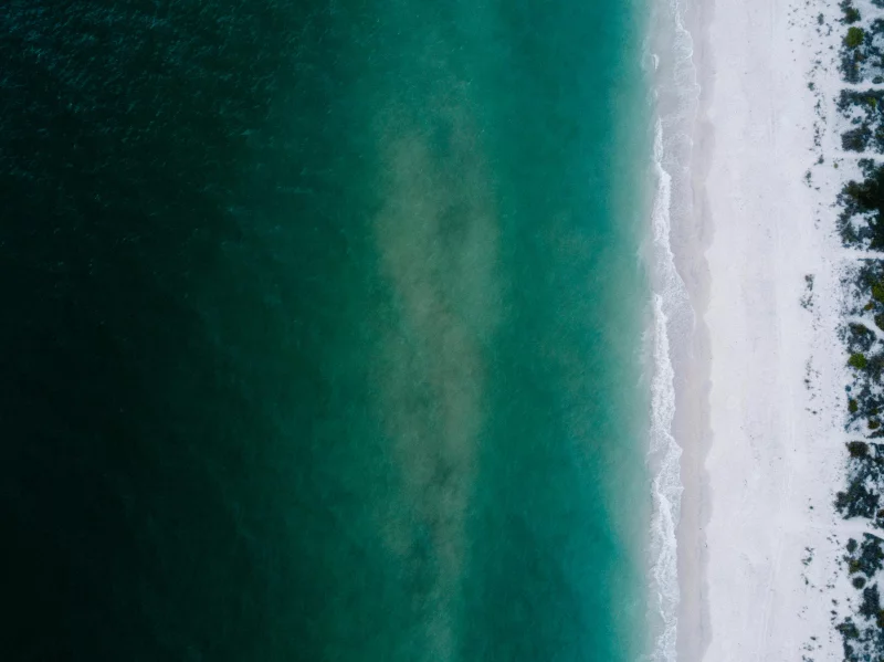 Stunning aerial shot of a serene beach with clear turquoise water blending into white sand.