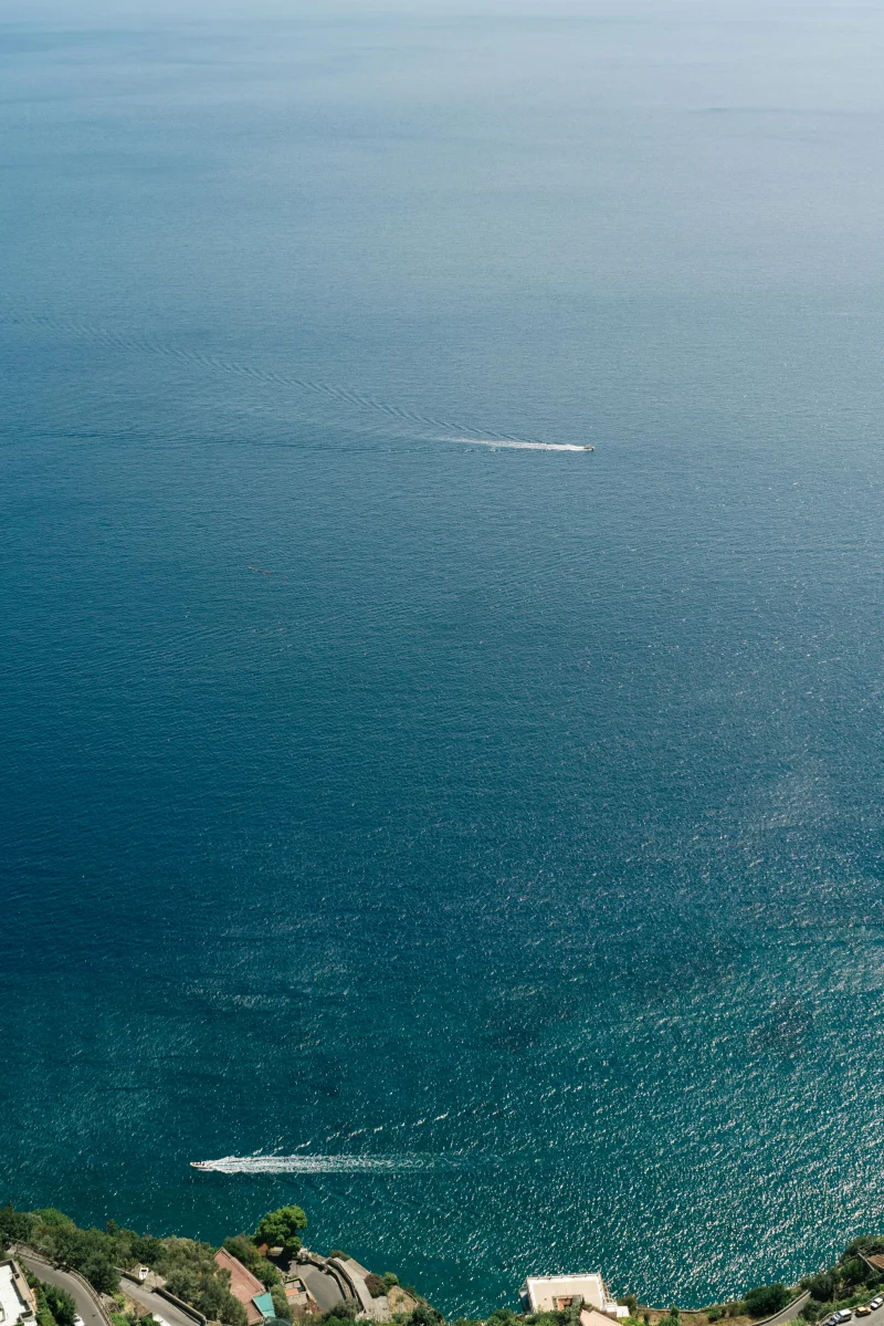 A stunning aerial view of the tranquil Amalfi coast with boats sailing on the blue Mediterranean Sea.