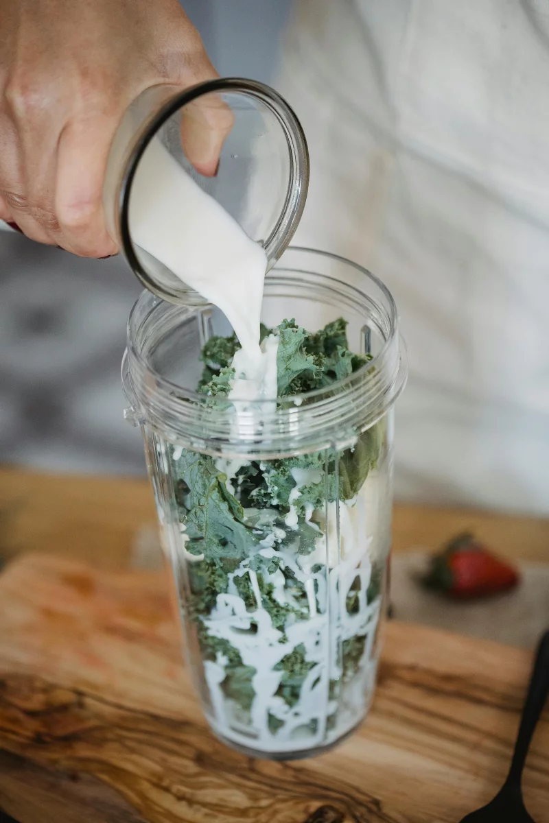 Fresh milk being poured into a blender with kale for a nutritious smoothie.