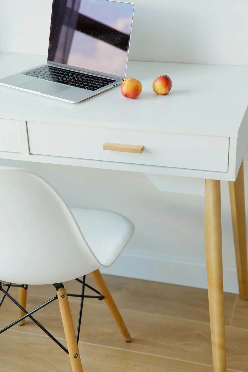 Modern minimalist workspace featuring a sleek laptop and two fresh apples on a white desk with a white chair.