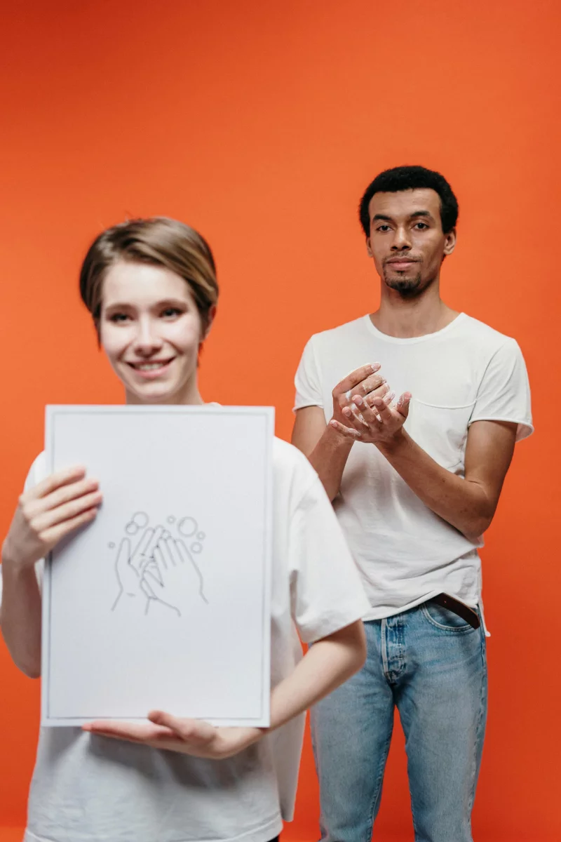 Two people emphasize the importance of hand hygiene against a vibrant orange background.