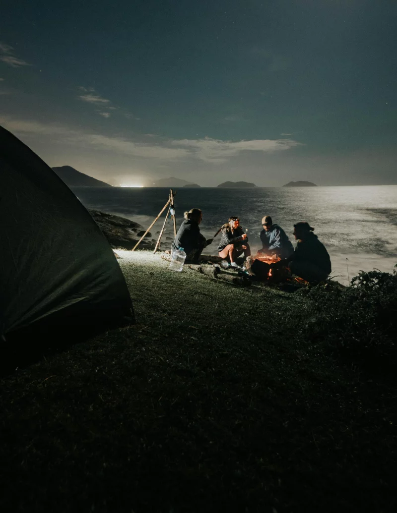 A group enjoying a campfire at a seaside campsite under the night sky.