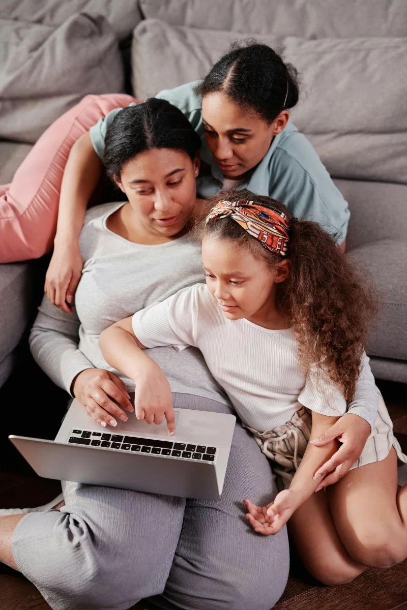 A family of three sharing happy moments using a laptop together on the couch.