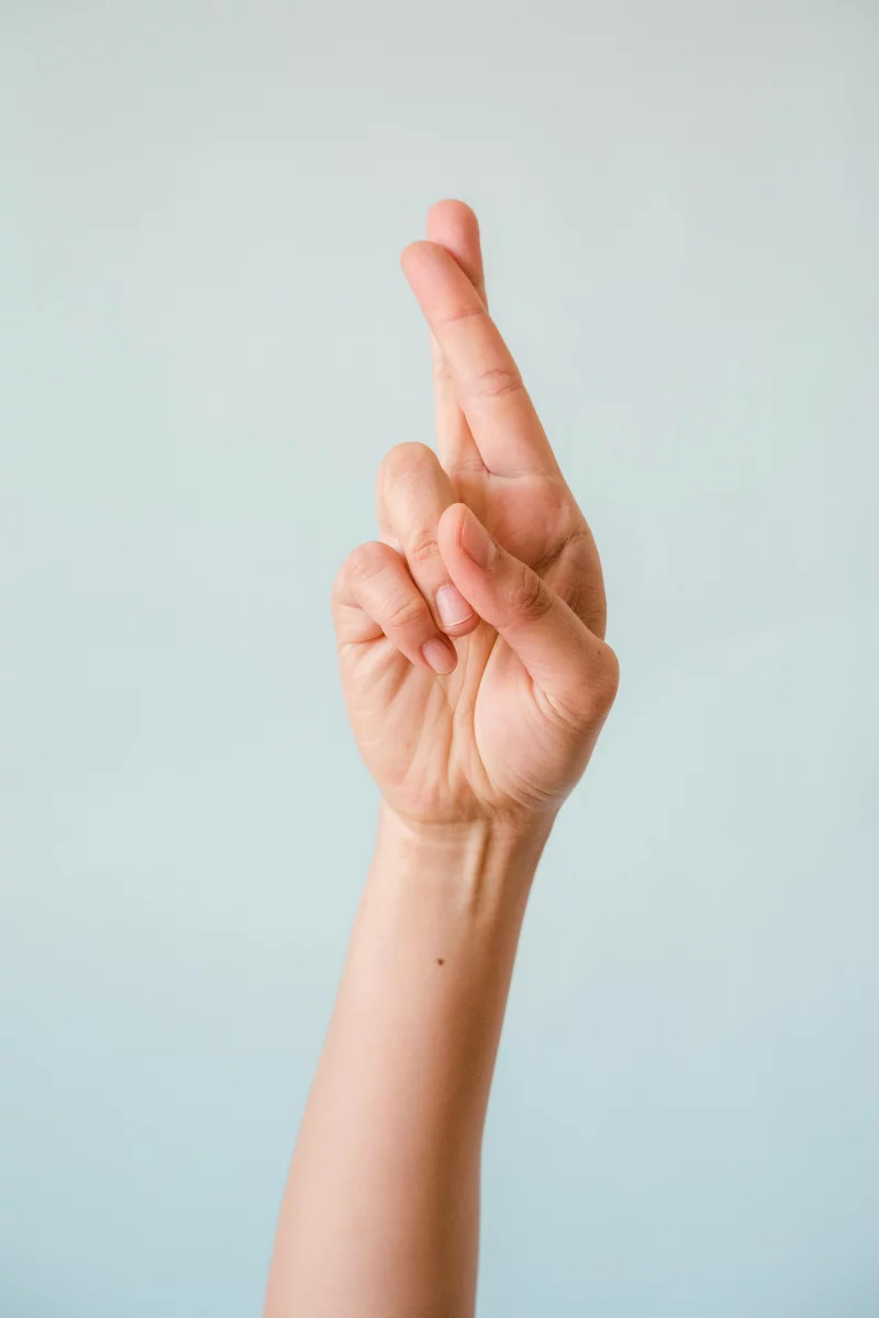 Close-up of a hand with fingers crossed against a soft blue background, representing hope and luck.