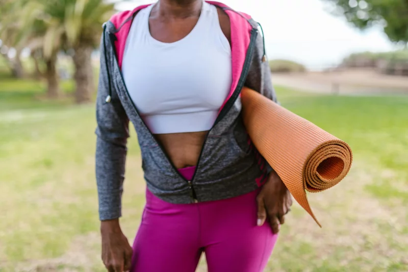 Close-up of an African American woman holding a yoga mat outdoors, promoting active lifestyle.