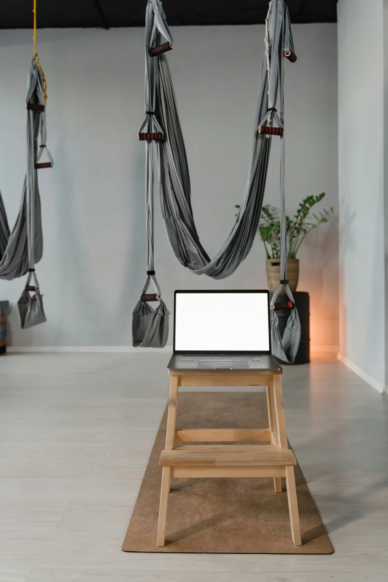 A serene yoga studio featuring aerial hammocks and a blank laptop, emphasizing modern fitness and technology integration.