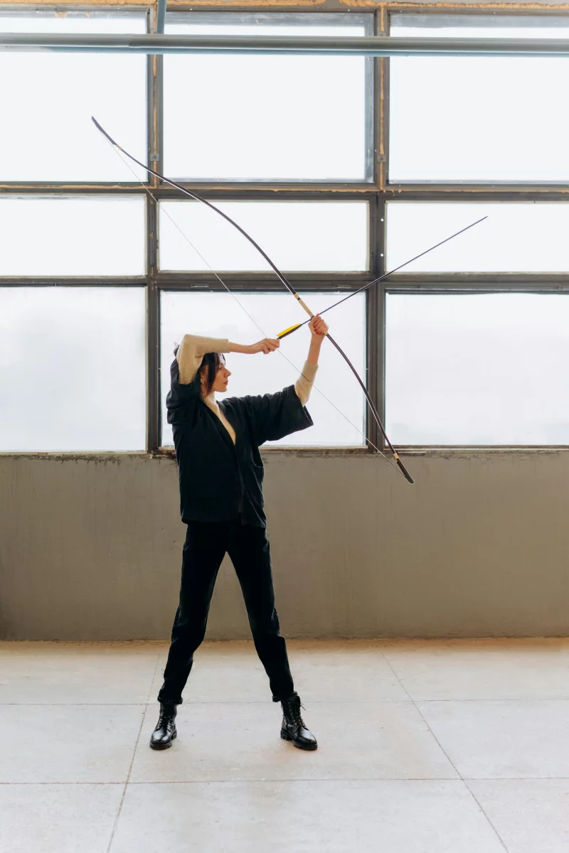 Woman holding a bow indoors, showcasing focus and determination in archery practice.