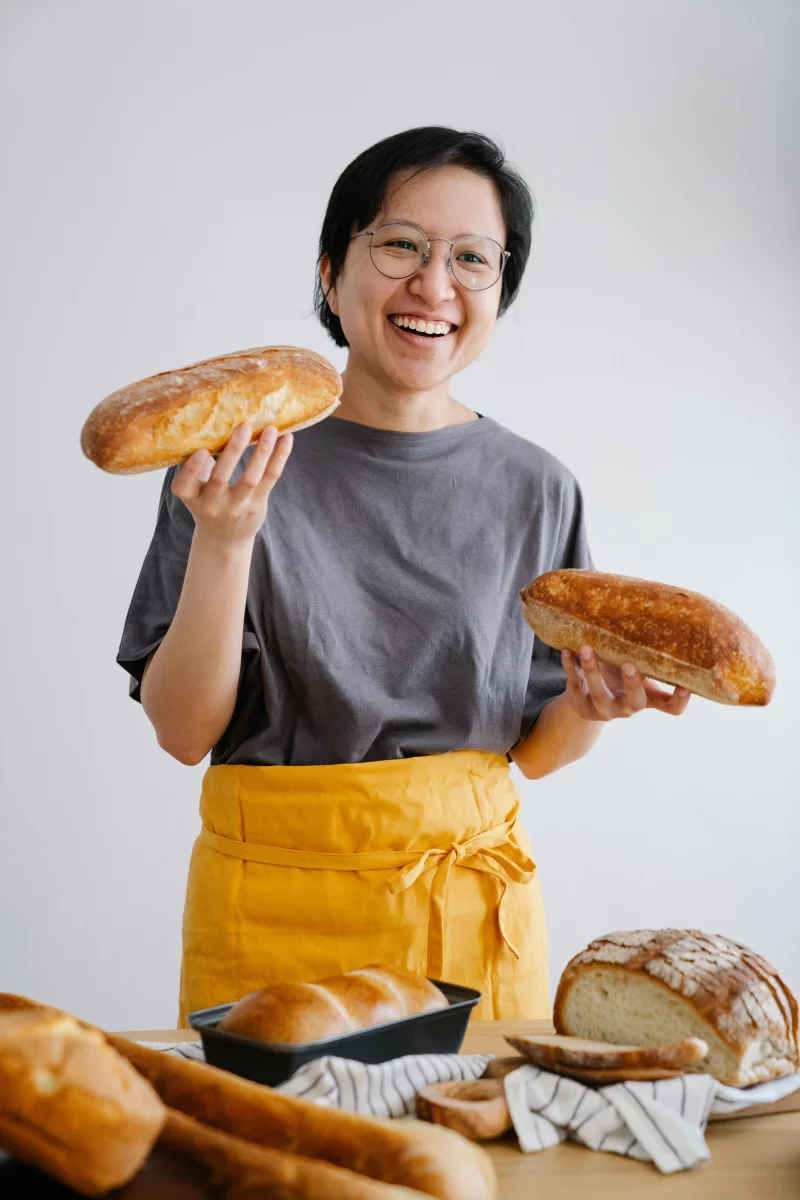 A cheerful baker proudly displays freshly baked loaves in a warm, inviting kitchen setting.