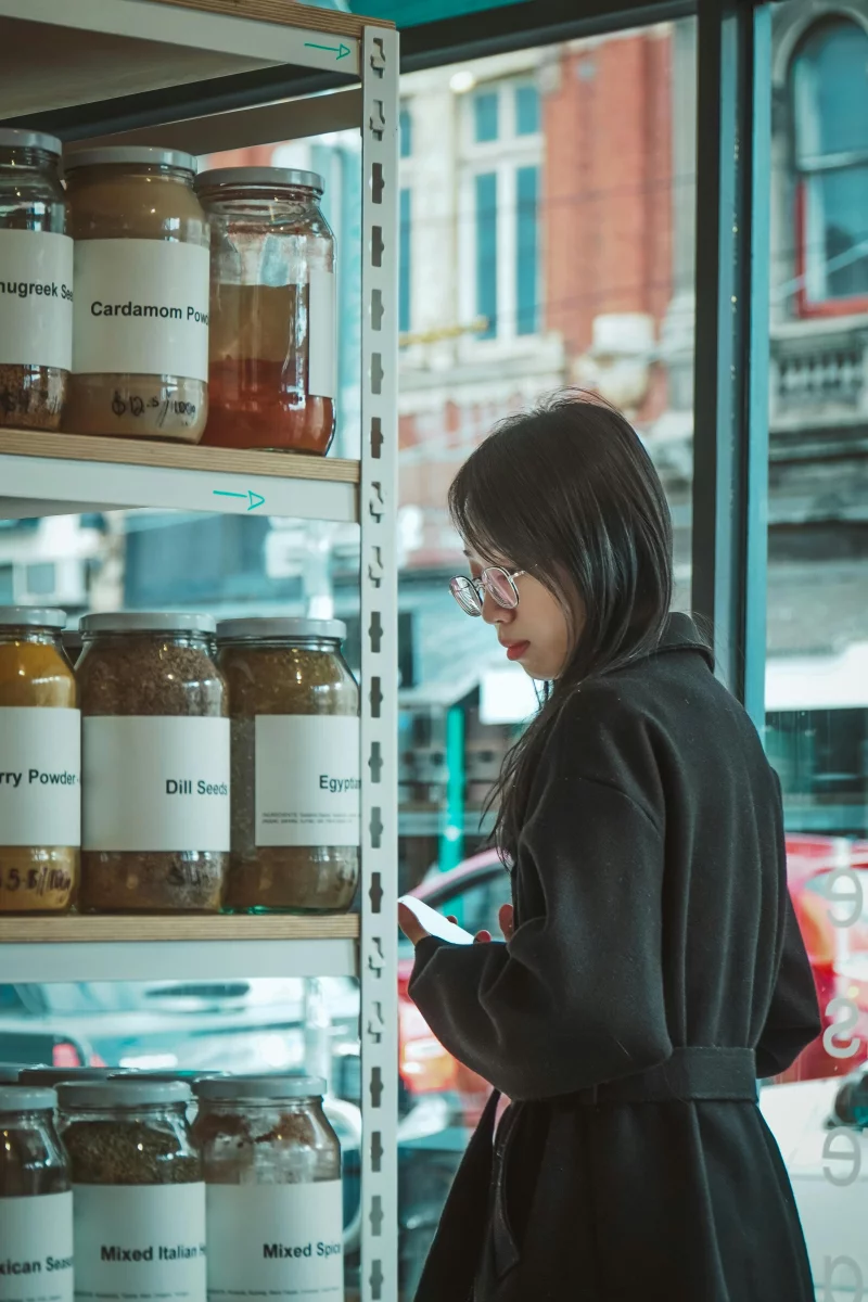 A woman with eyeglasses examines jars in a modern indoor store setting.