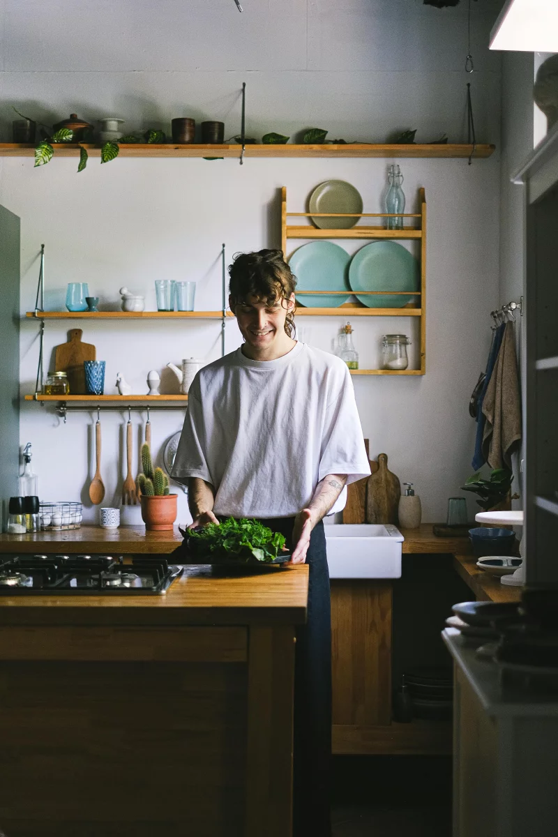 A person smiles while preparing fresh ingredients in a cozy kitchen.