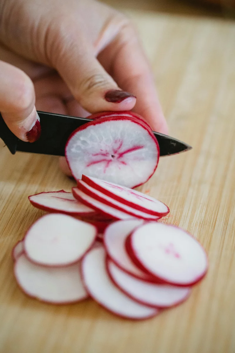 Detailed close-up of a hand slicing radish on a wooden board with a knife.