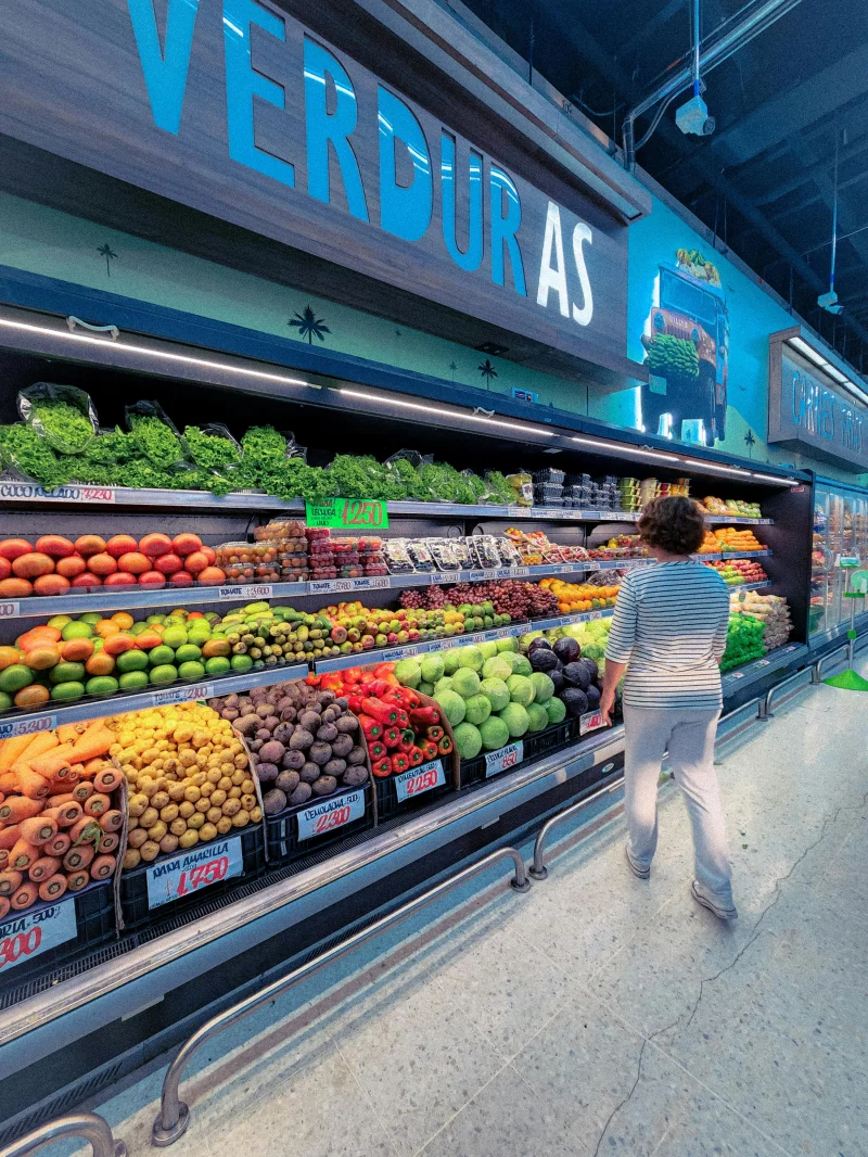 Woman browsing fresh fruits and vegetables in a supermarket aisle.