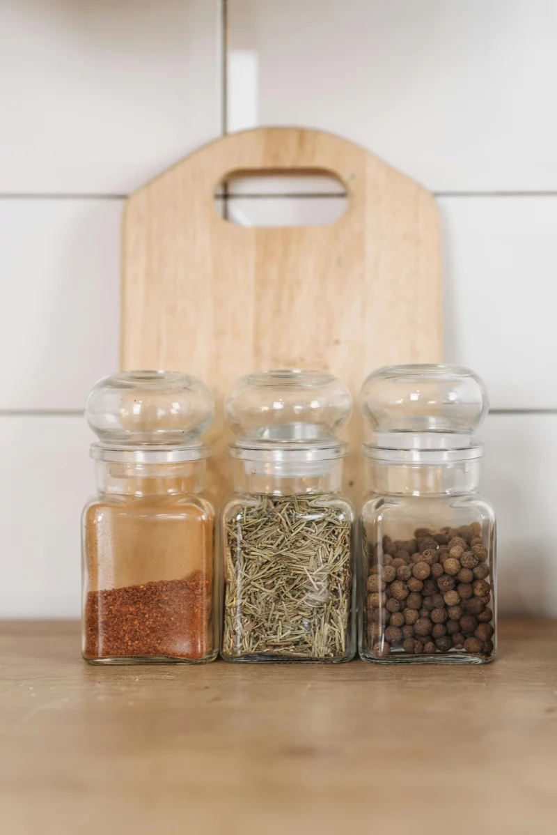 Close-up of glass jars filled with assorted spices and herbs on a wooden cutting board.
