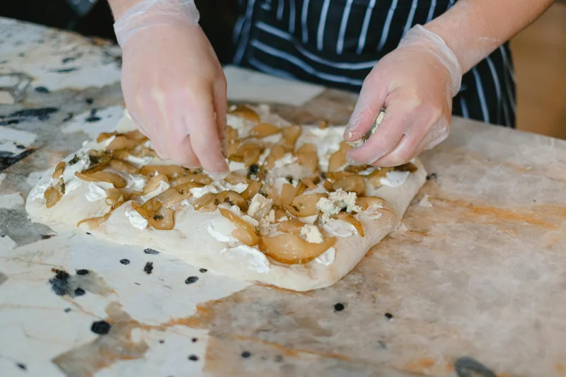 Hands preparing pear and cheese focaccia on a marble counter with gloves.