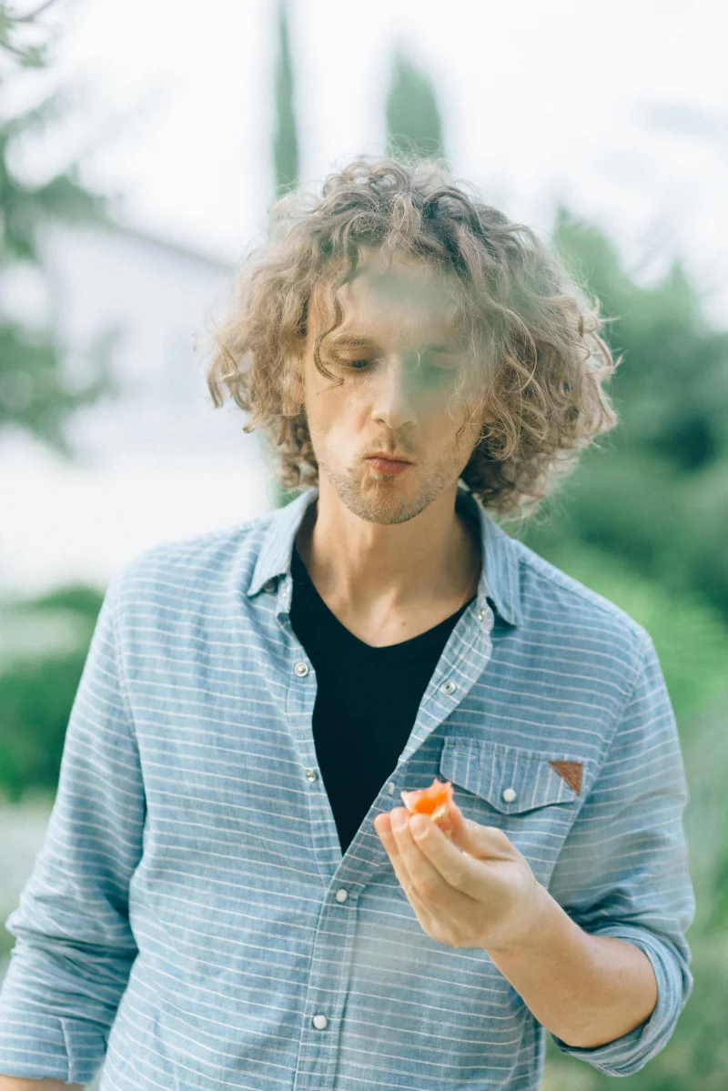 Young man savoring a slice of fresh tomato in a garden setting. Ideal for health or lifestyle themes.