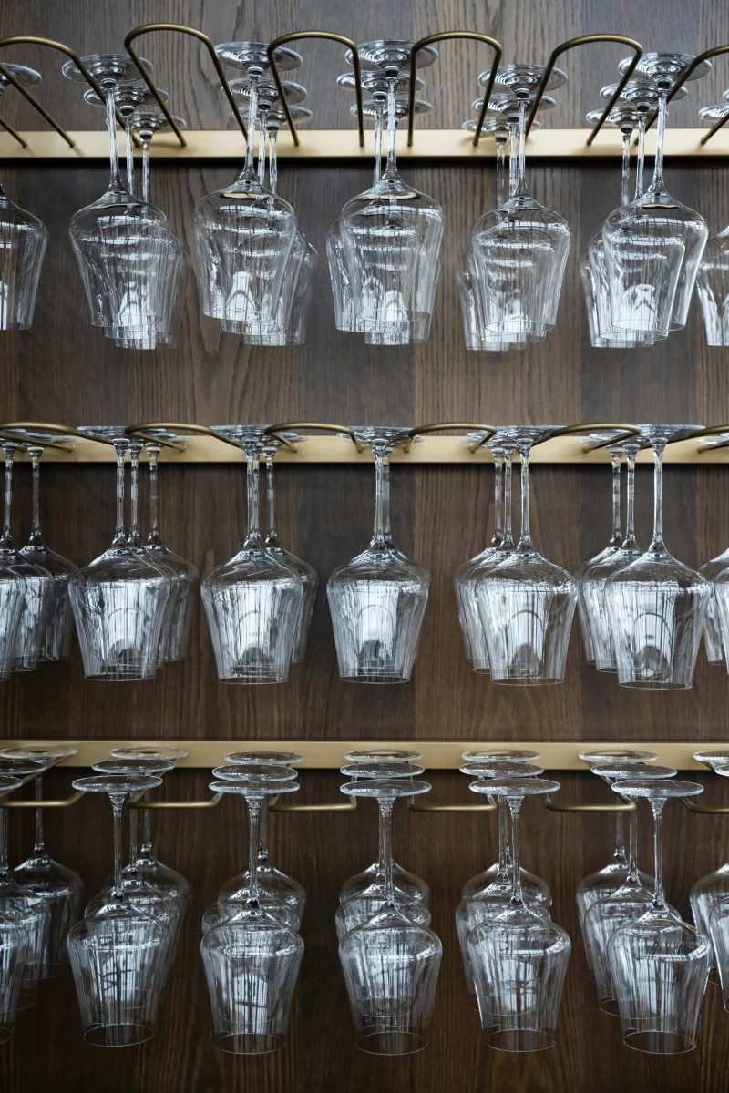 Neatly arranged wine glasses hanging upside down on a stylish wooden rack.