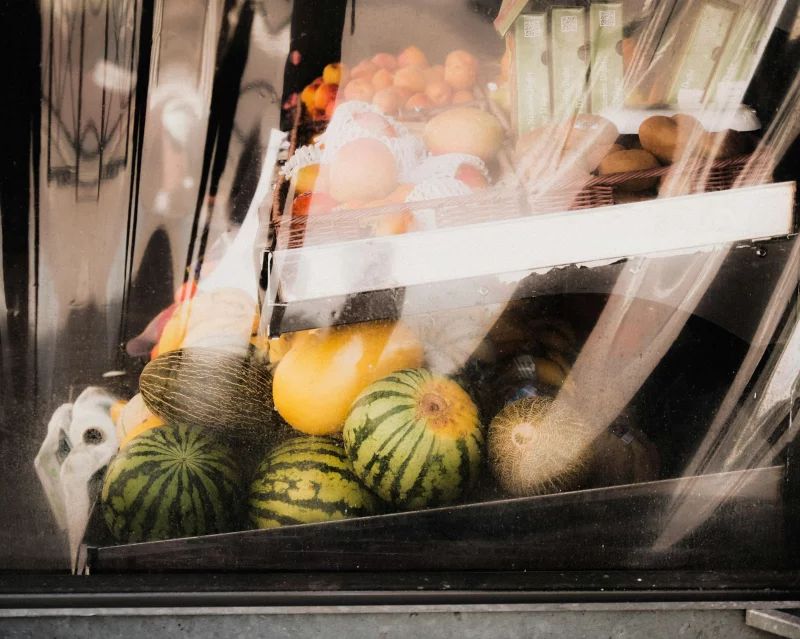A vibrant array of fresh fruits including melons and oranges displayed in a shop window.