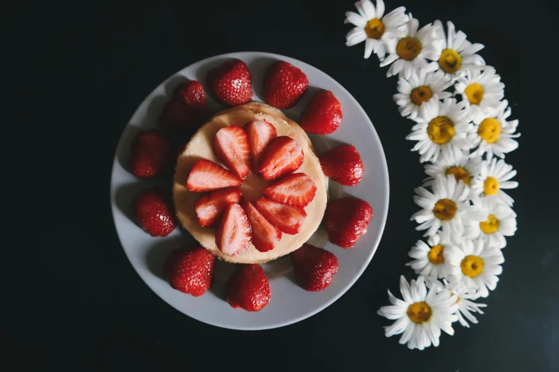 A top view of a delicious pancake adorned with fresh strawberries and surrounded by daisies.