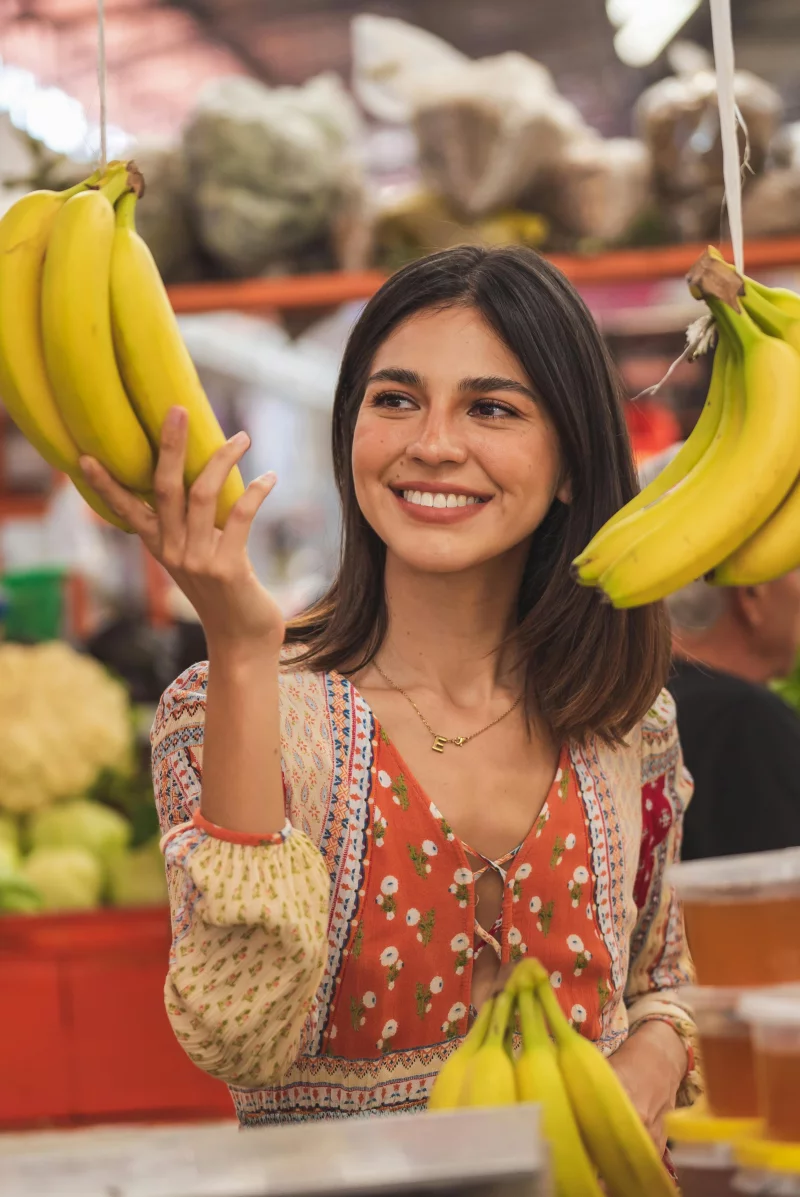 Woman enjoying shopping for bananas at a vibrant indoor market. Capturing the joy of fresh produce.