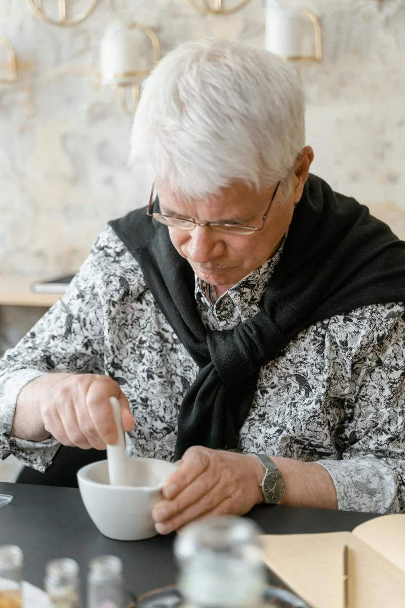 Senior man with white hair using a mortar and pestle. Indoors setting, focusing on traditional method.