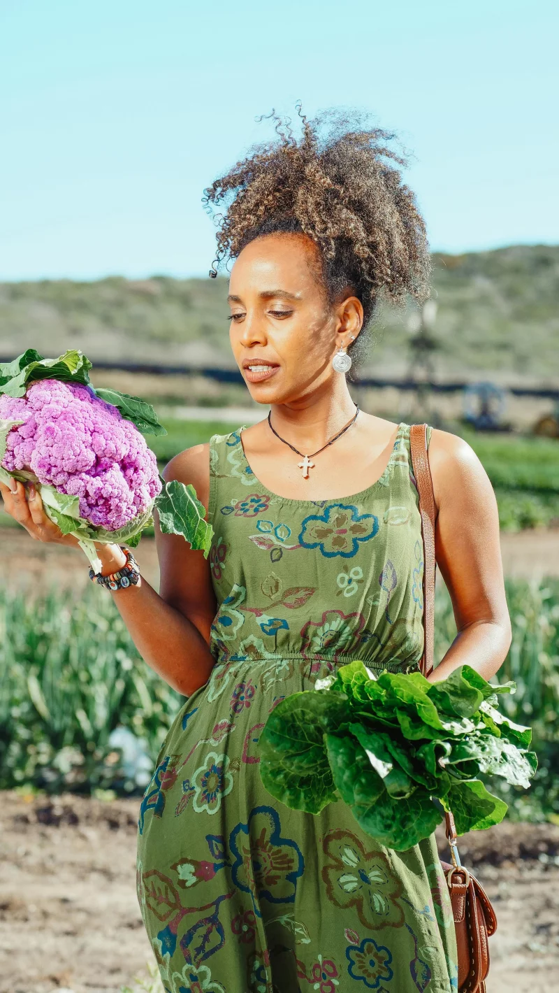 African American woman holding fresh cauliflower and lettuce on a farm in summer.