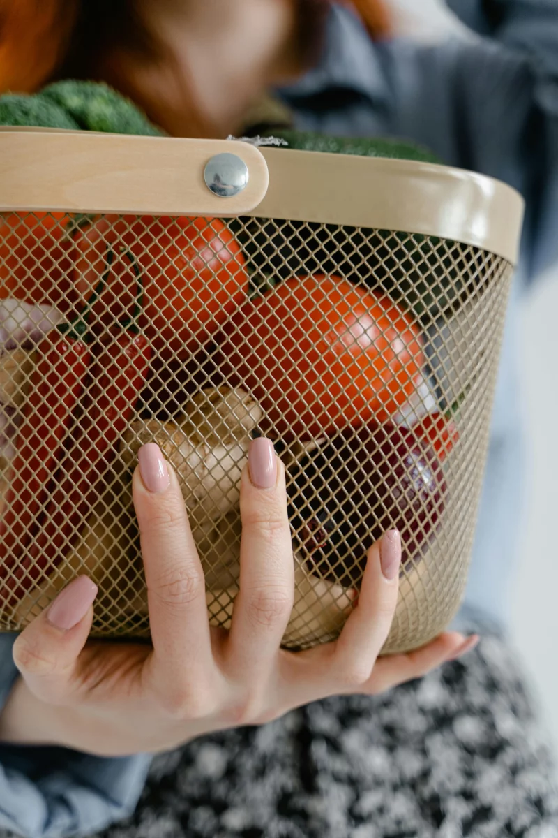 A person holding a wire basket filled with fresh vegetables like tomatoes and peppers. Perfect for food and grocery themes.