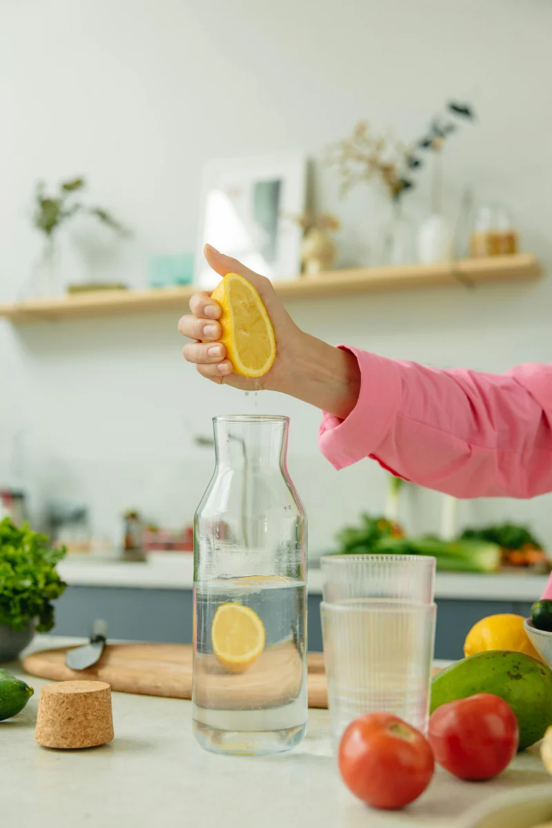 A person holds a lemon over a glass pitcher in a modern kitchen, preparing fresh juice.
