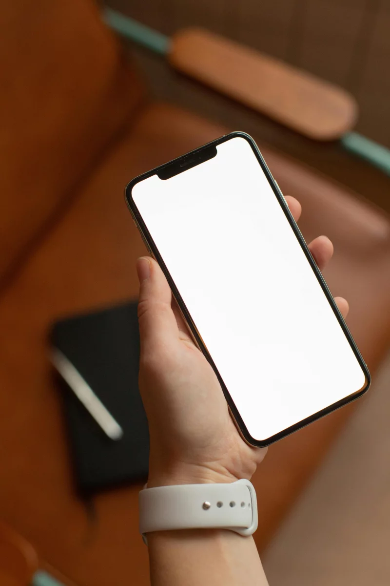 A hand holding a smartphone with a blank screen inside a brown leather chair setting.