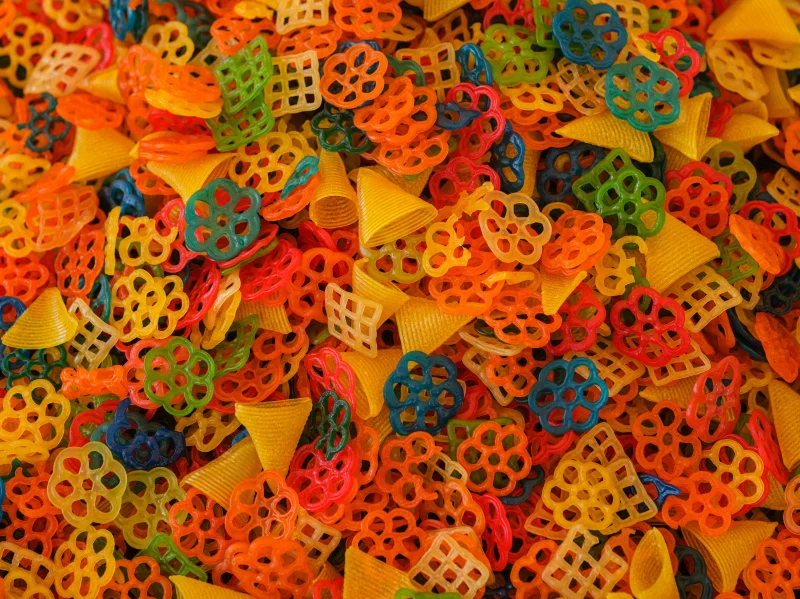A colorful assortment of various uncooked pasta shapes, showcasing bright hues and unique designs.