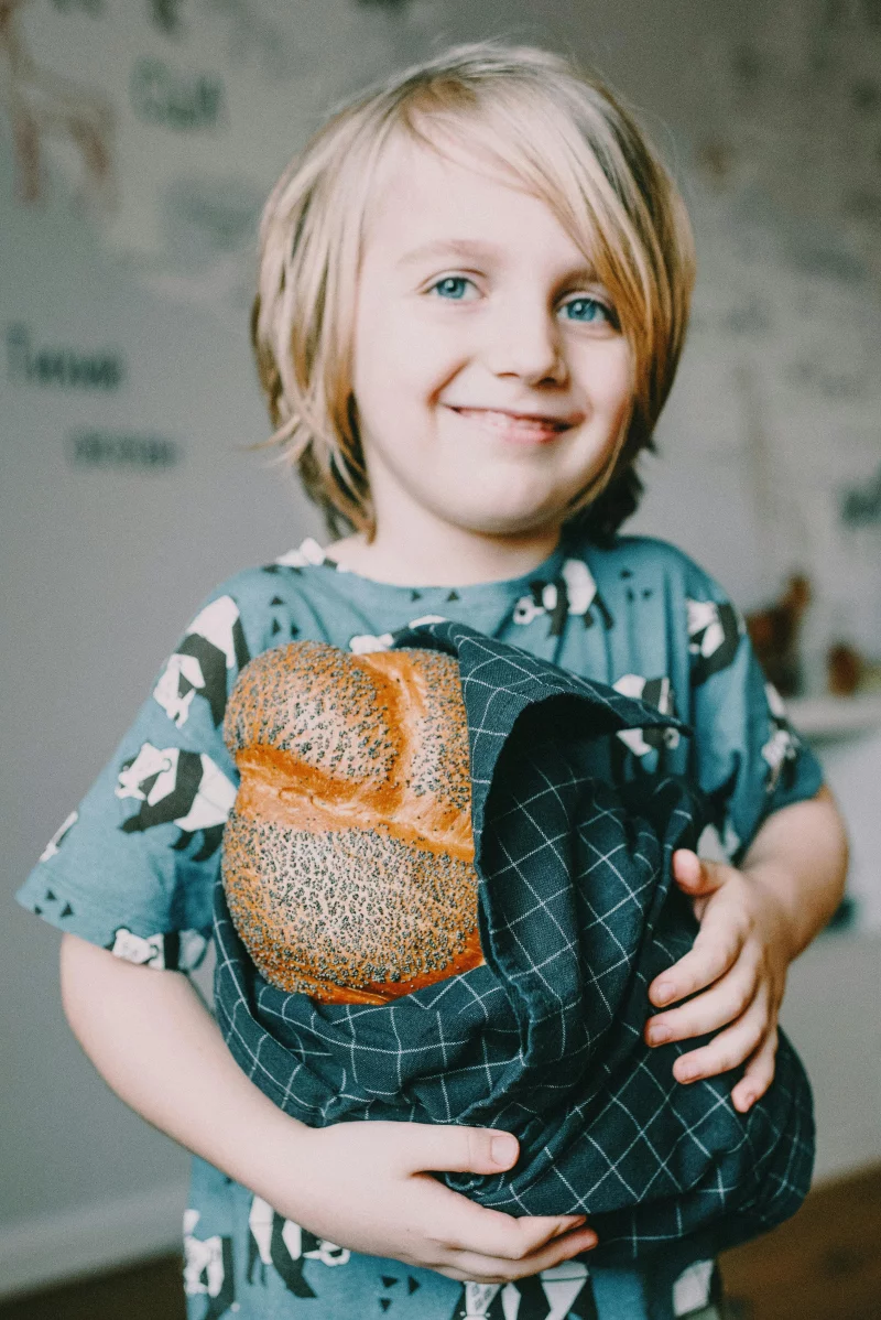 Happy young child holding a loaf of traditional bread indoors. Warm and inviting atmosphere.